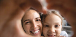 Smiling Hispanic Mom And Biracial Daughter Show Heart Sign