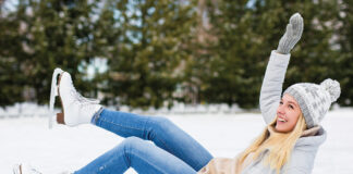 Young Woman Falling Down While Ice Skating At Winter Rink