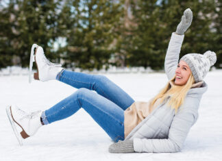 Young Woman Falling Down While Ice Skating At Winter Rink