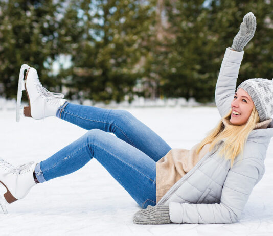 Young Woman Falling Down While Ice Skating At Winter Rink