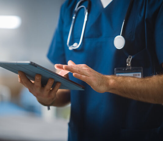 Hospital Ward: Unrecognizable Head Nurse, Doctor, Surgeon Uses Digital Tablet Computer Health Care Vitals Monitoring Computer Machine. Modern Clinic With Advanced Equipment And Professional Working