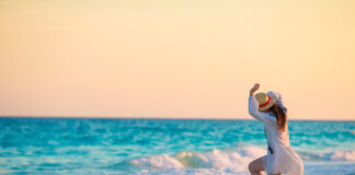 Young Beautiful Woman On Tropical Seashore In Sunset. Happy Girl In Dress In The Evening On The Beach