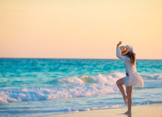 Young Beautiful Woman On Tropical Seashore In Sunset. Happy Girl In Dress In The Evening On The Beach