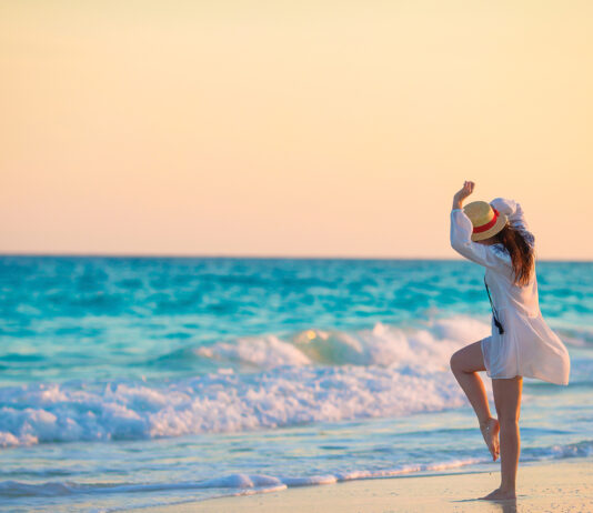 Young Beautiful Woman On Tropical Seashore In Sunset. Happy Girl In Dress In The Evening On The Beach