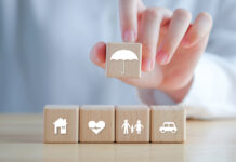 Insurance Concept. Protection Against A Possible Eventuality. Hand Holding Umbrella Icon And House, Car, Family And Health Icon On Wooden Block For Assurance Life Concept.