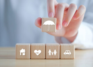 Insurance Concept. Protection Against A Possible Eventuality. Hand Holding Umbrella Icon And House, Car, Family And Health Icon On Wooden Block For Assurance Life Concept.