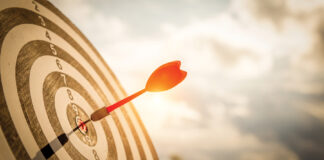 Close Up Shot Red Darts Arrows In The Target Of Dartboard Center On Dark Blue Sky Background. Business Target Or Goal Success And Winner Concept.