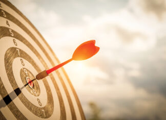 Close Up Shot Red Darts Arrows In The Target Of Dartboard Center On Dark Blue Sky Background. Business Target Or Goal Success And Winner Concept.