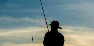 Silhouette Of Fishermen With Their Fishing Rods On The Rocks In Search Of Fish.