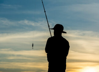 Silhouette Of Fishermen With Their Fishing Rods On The Rocks In Search Of Fish.