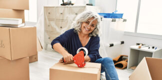 Middle Age Grey Haired Woman Smiling Happy Packing Kitchen Cardboard Box At New Home.