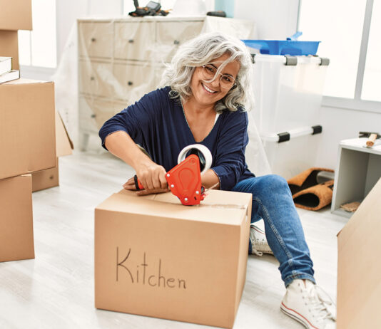 Middle Age Grey Haired Woman Smiling Happy Packing Kitchen Cardboard Box At New Home.