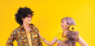 Asian Hippie Couple Dress In 80s Vintage Fashion With Colorful Retro Clothing While Dancing Together Isolated On Yellow Background For Fancy Outfit Party And Pop Culture