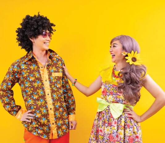 Asian Hippie Couple Dress In 80s Vintage Fashion With Colorful Retro Clothing While Dancing Together Isolated On Yellow Background For Fancy Outfit Party And Pop Culture